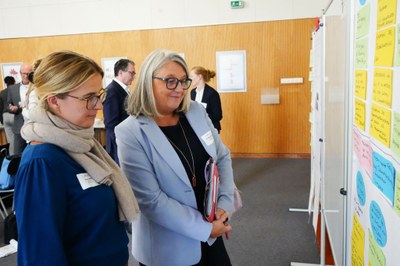 Veranstaltung Personen Zwei Personen stehen im einem Veranstaltungsraum vor einem Whiteboard mit beschriebenen Zetteln